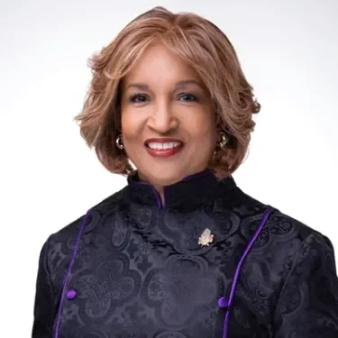 Portrait of a woman with blonde hair smiling, wearing a dark purple traditional Asian dress with intricate patterns and purple accents.