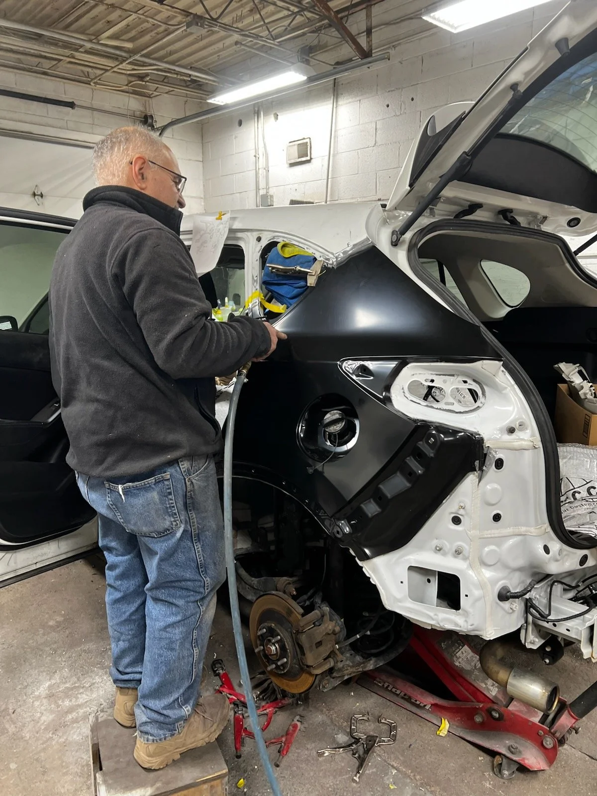 A man working on the rear of a car in a workshop, with the rear wheel removed and the brake rotor exposed.
