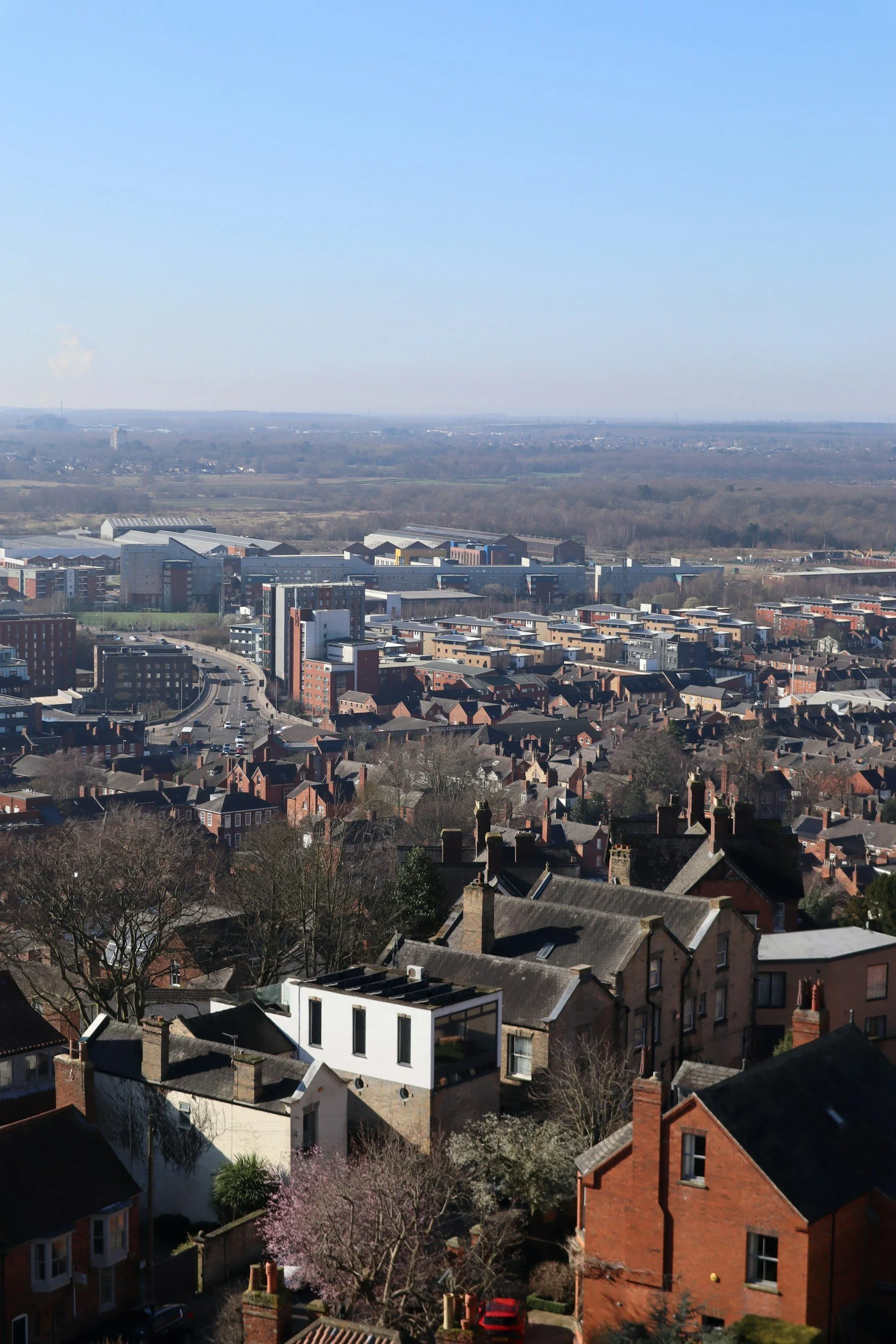 A cityscape view with a mix of residential and commercial buildings, roads, and open land in the background under a clear blue sky.