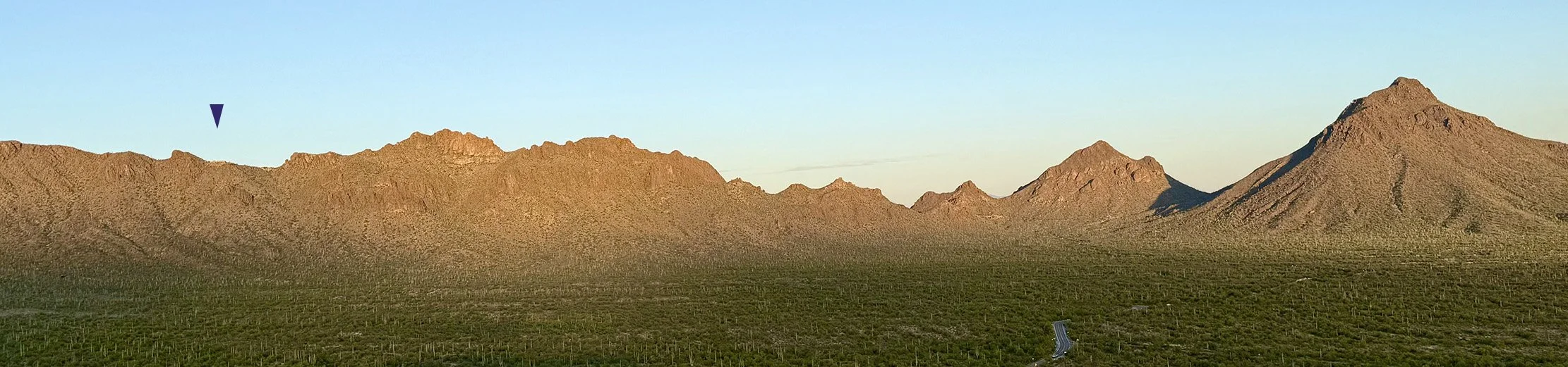 A desert landscape with distant mountain ranges under a clear blue sky.