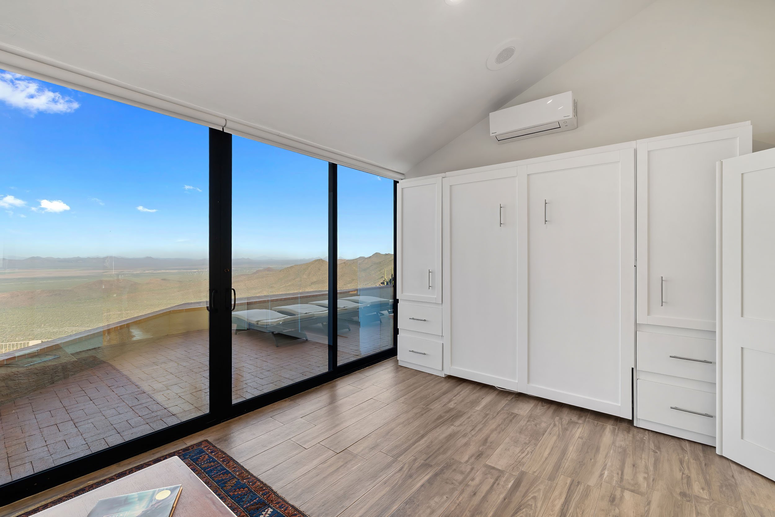 Living room with floor-to-ceiling windows offering a mountain and desert view, white built-in cabinets, and light wood flooring.