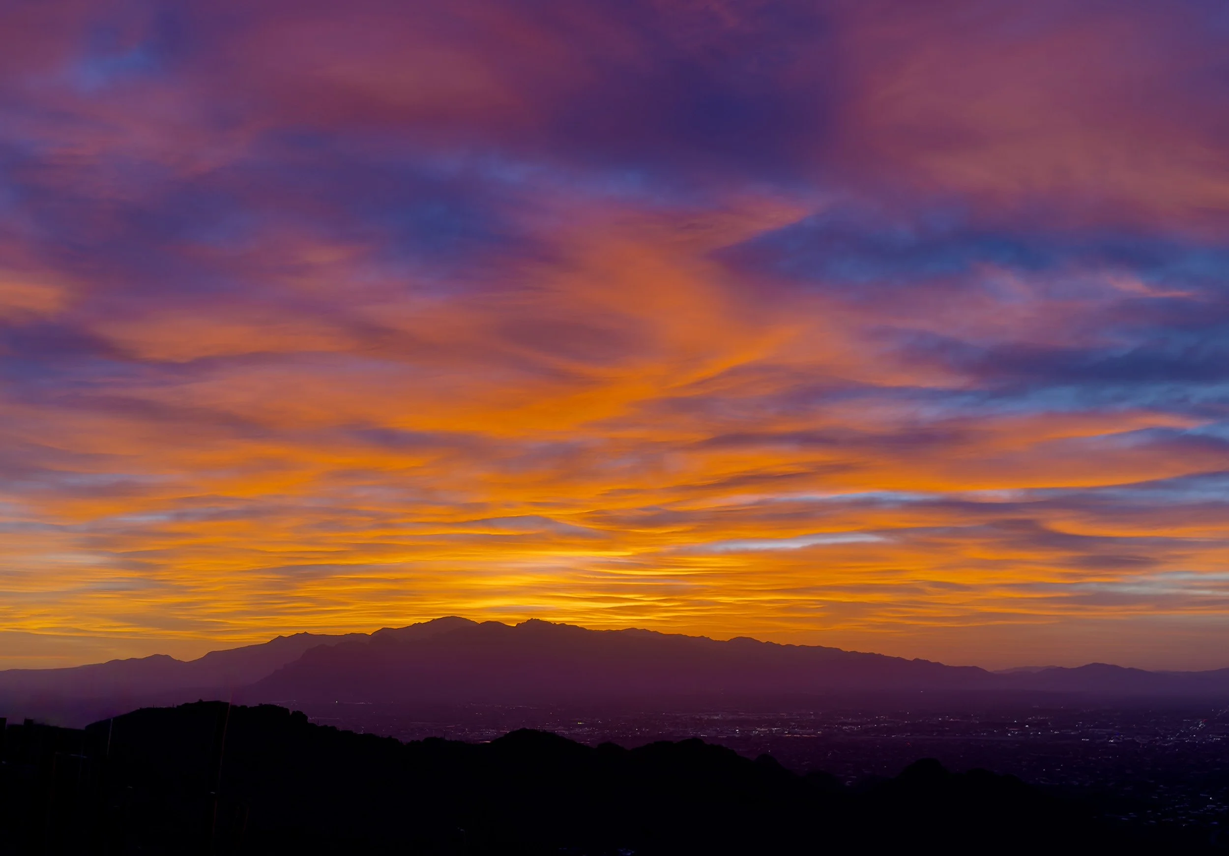 A vibrant sunset sky with shades of purple, pink, orange, and yellow over mountain silhouettes on the horizon.