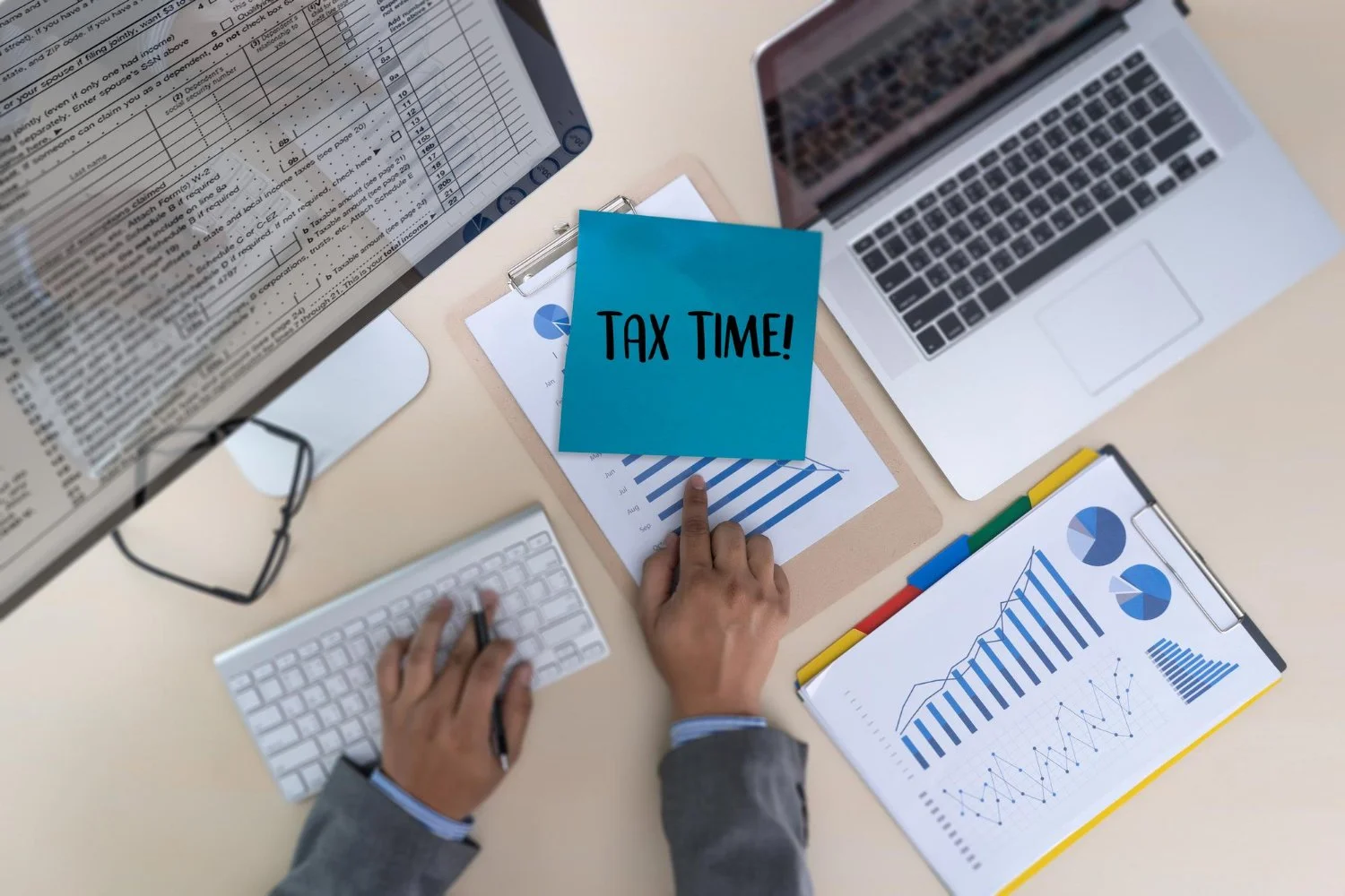 Desk with tax documents, charts, a laptop, a keyboard, and a blue paper that reads 'TAX TIME!'