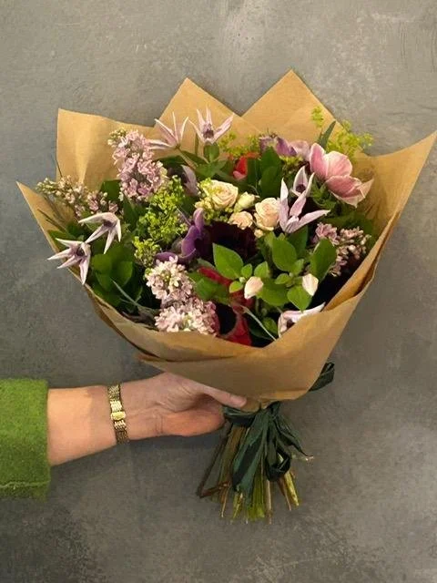 A bouquet of Clematis, Roses, Hellebores and Lilac wrapped in craft paper.