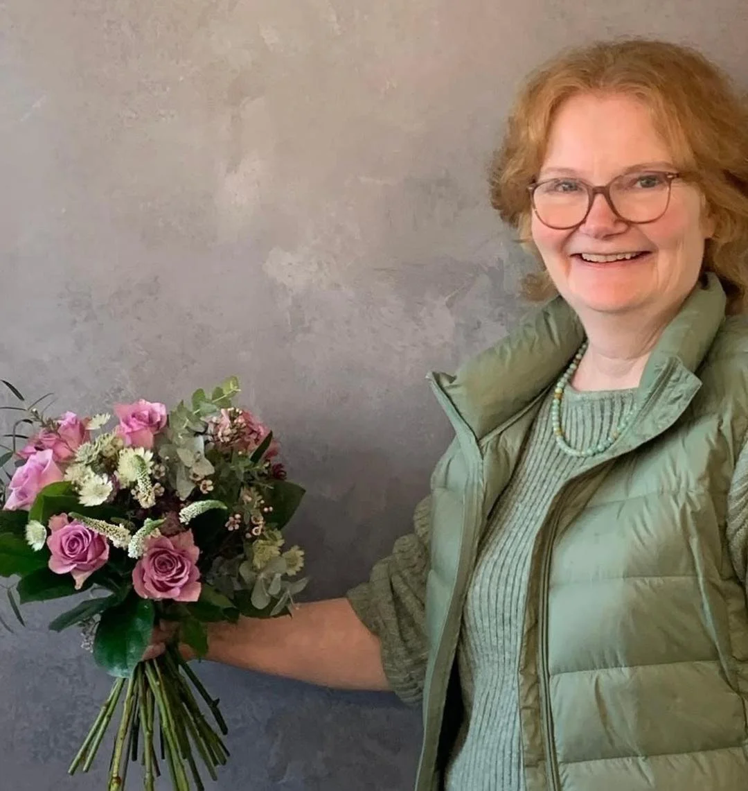 A lady holding a handtied wedding bouquet in pinks and cream with foliage.