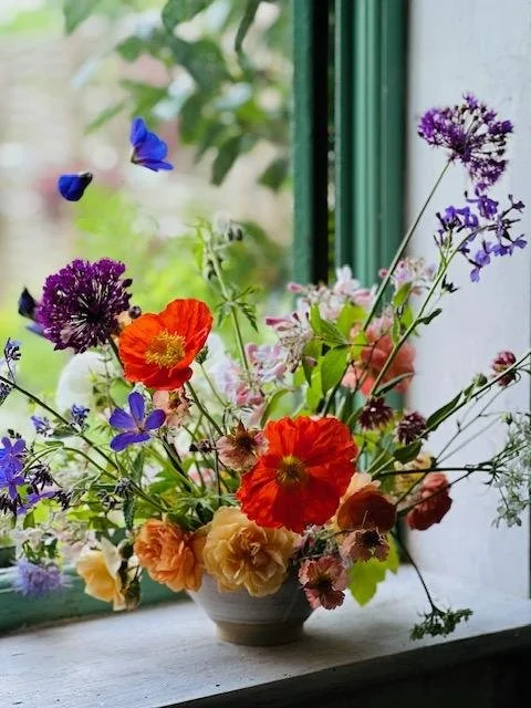 A bowl on a window ledge filled with bright summer flowers