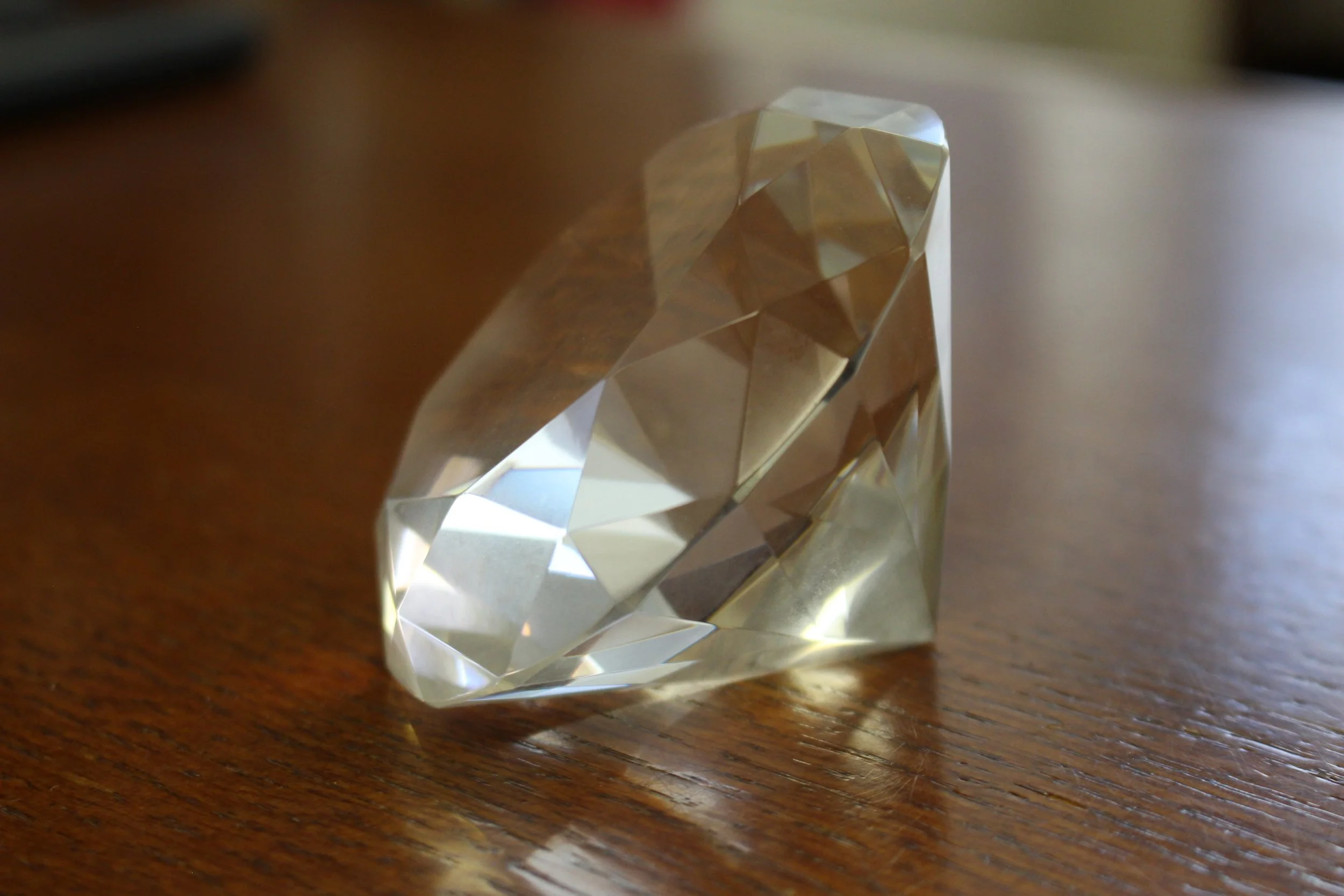 Close-up of a clear, multi-faceted, gem-like object on a wooden surface, reflecting light.