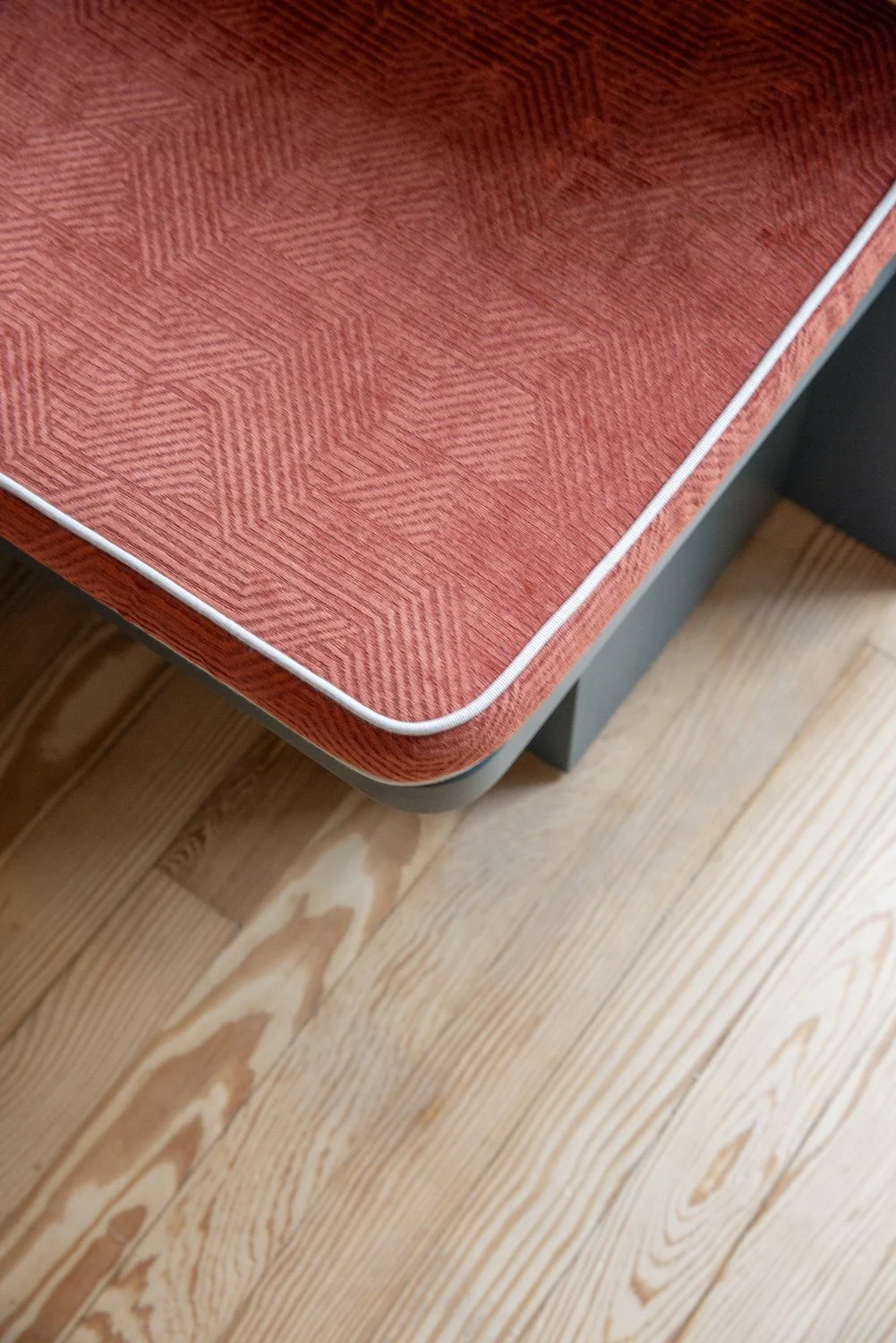 Table en bois avec un revêtement rouge à motifs géométriques, bordure blanche, placé sur un sol en bois naturel clair.
