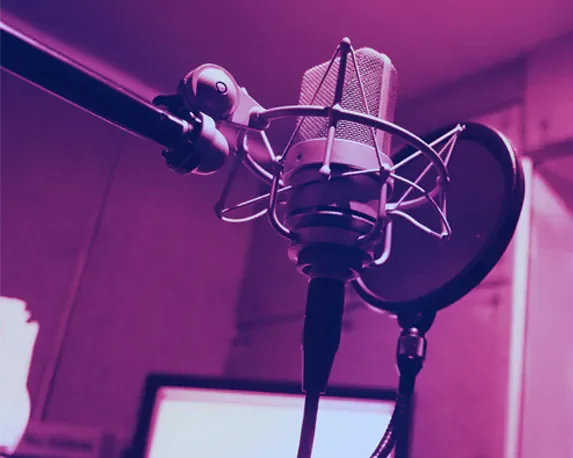 Close-up of a professional studio microphone with a pop filter, mounted on a boom arm, in a recording studio with purple lighting.
