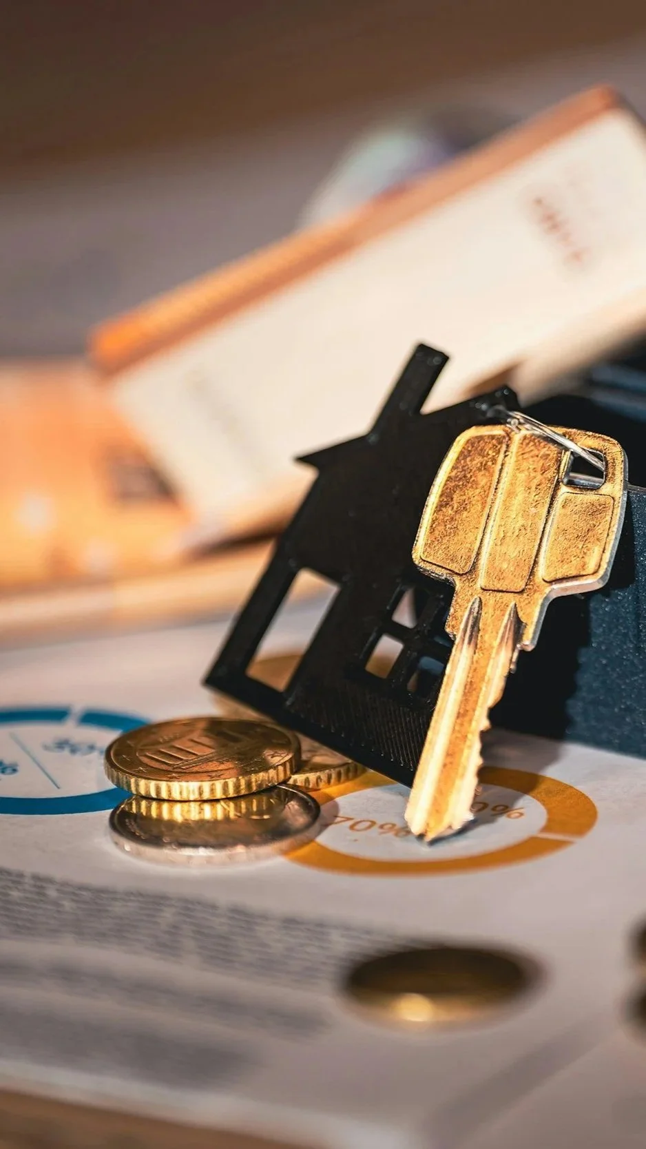 A gold key, black plastic house-shaped keychain, some gold coins, and a document with printed text and colorful charts placed on a surface.