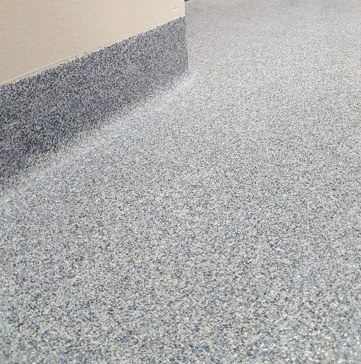 Close-up of a speckled, gray and white textured flooring next to a beige wall.