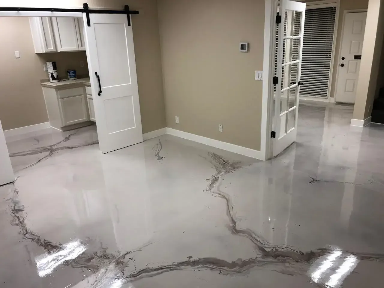 Living room with shiny, polished marble floors with dark veining, beige walls, a white sliding barn door, glass-paneled French doors, and a partially visible kitchen.