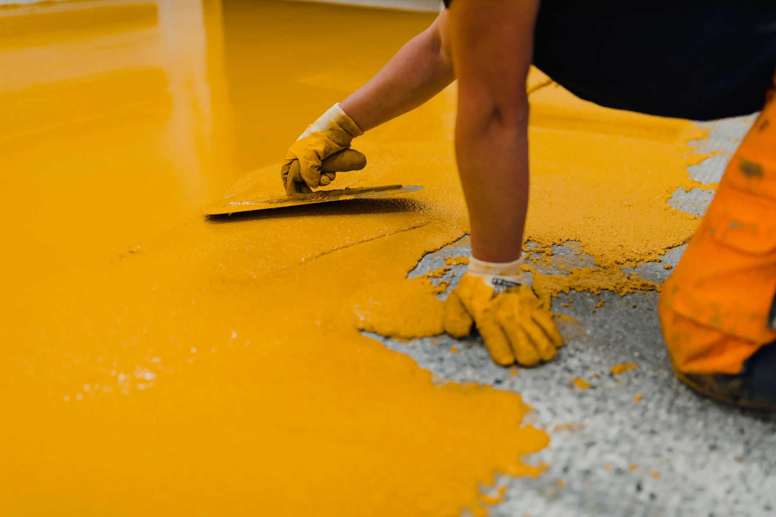 A person using a trowel to spread yellow paint on a surface.