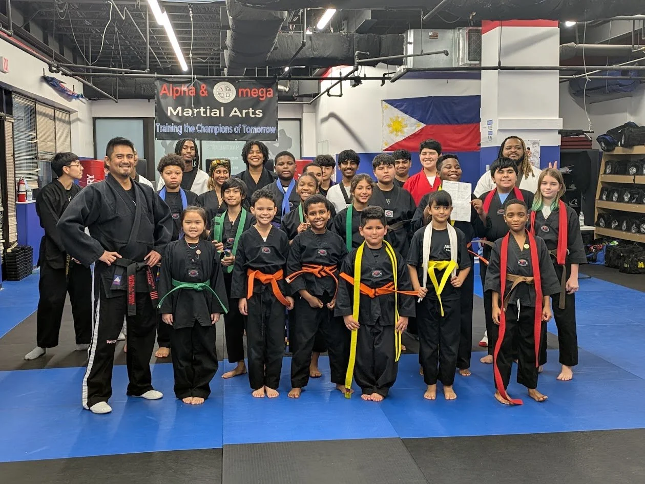 Alpha and Omega students and instructors on the mats in Laurel, with the school banner and the flag of the Philippines behind them.