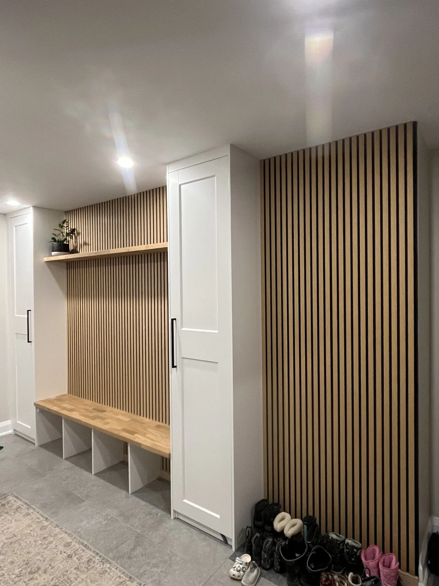 Frozen shoe storage area with shoes and socks at the bottom, white cabinetry, and decorative wooden slat wall panels.