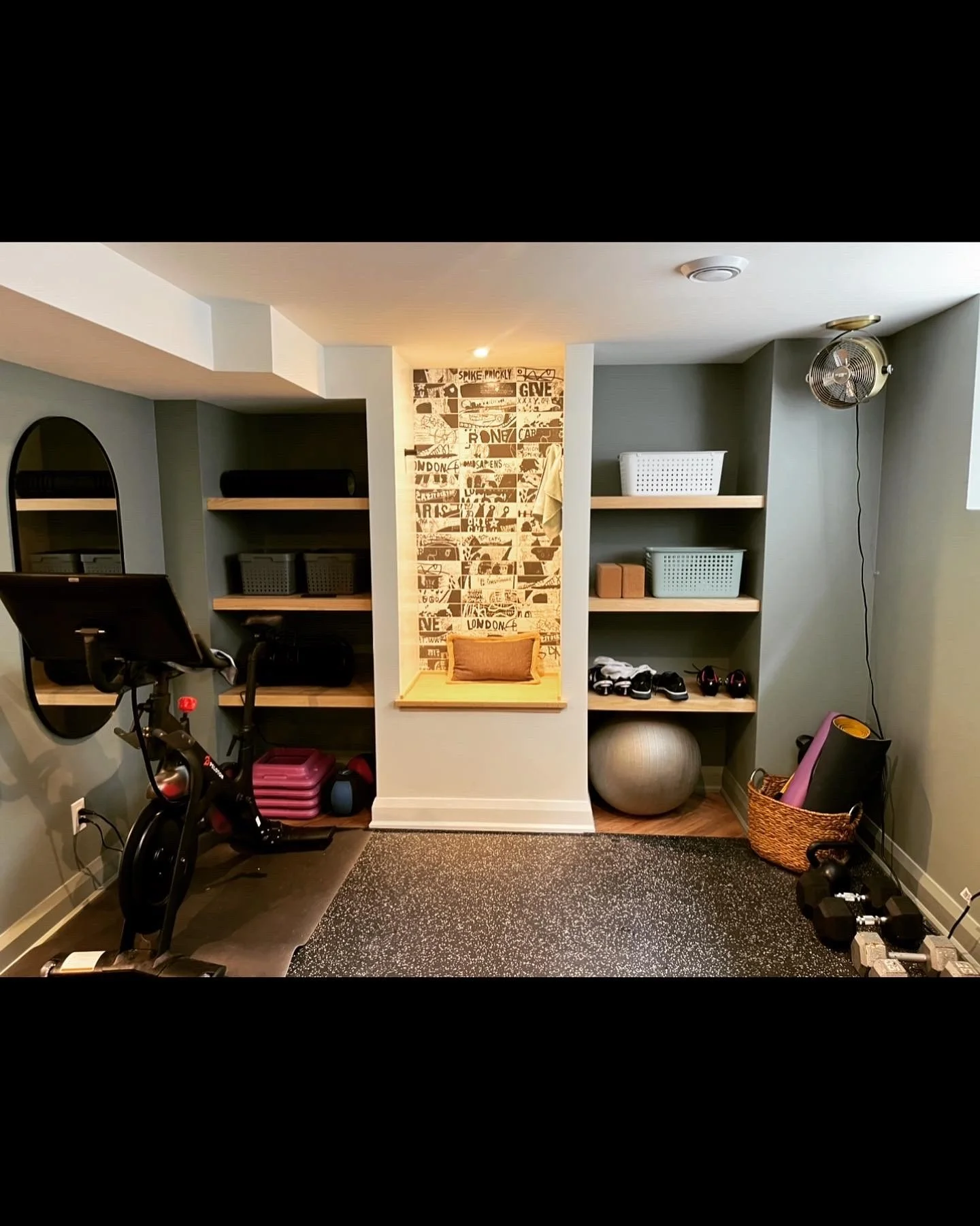 Home gym with shelves containing exercise equipment, bike, stability ball, yoga mat, dumbbells, and a small nook with a cushion.
