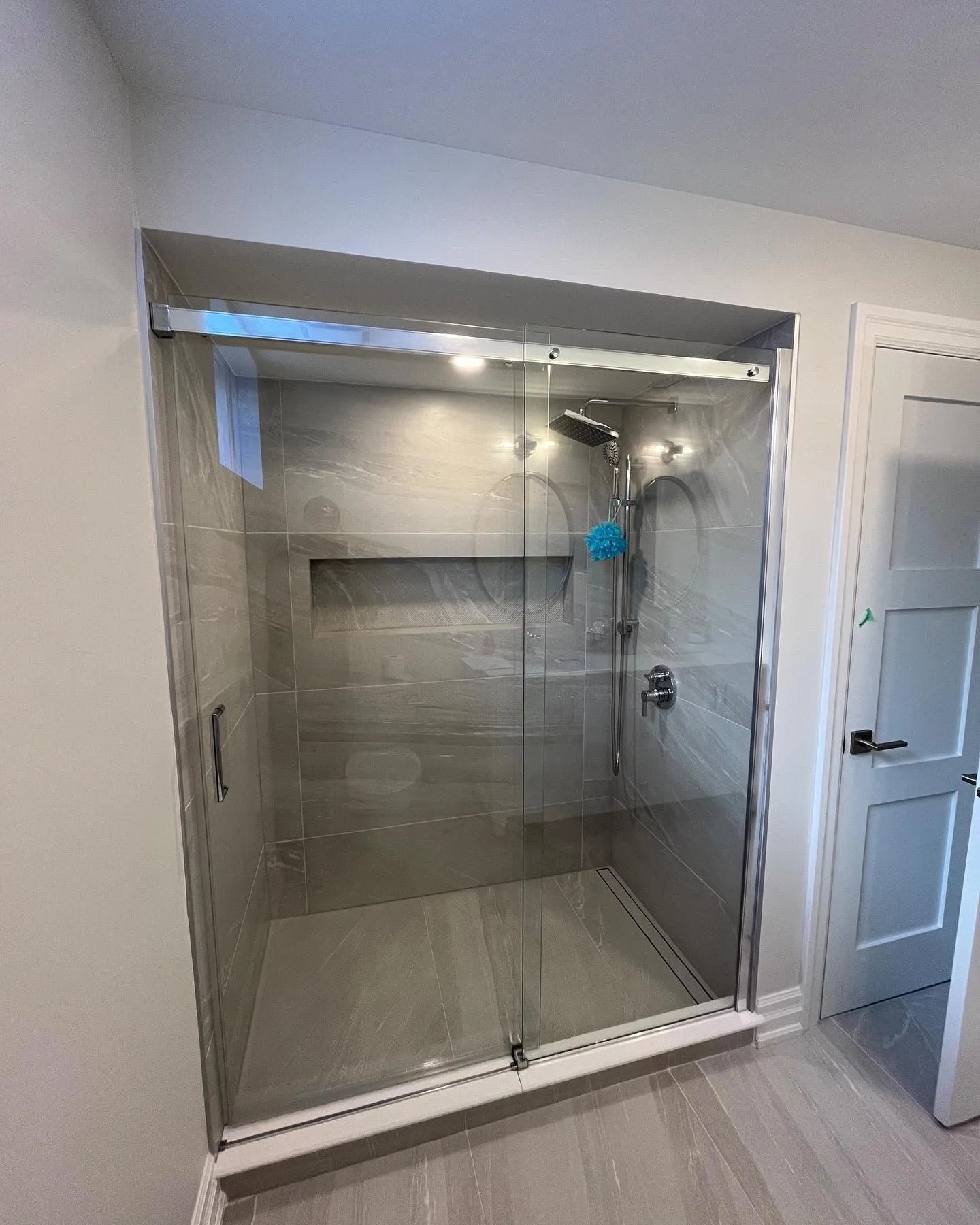 A modern walk-in shower with glass doors, gray marble tiles on the walls and floor, a rainfall showerhead, and a small built-in bench or shelf.