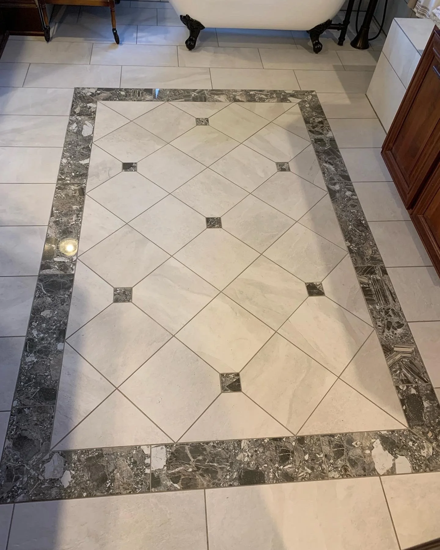 Decorative tile floor with a central pattern of white tiles, bordered by a dark, marbled border, in a room with beige walls and furniture.