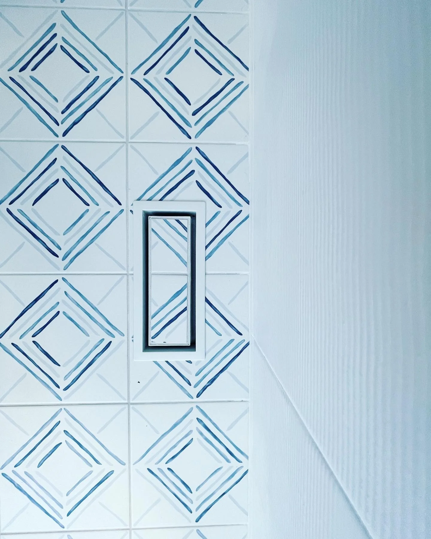 A wall with decorative tiles featuring blue geometric patterns and a rectangular metal handle or fixture.