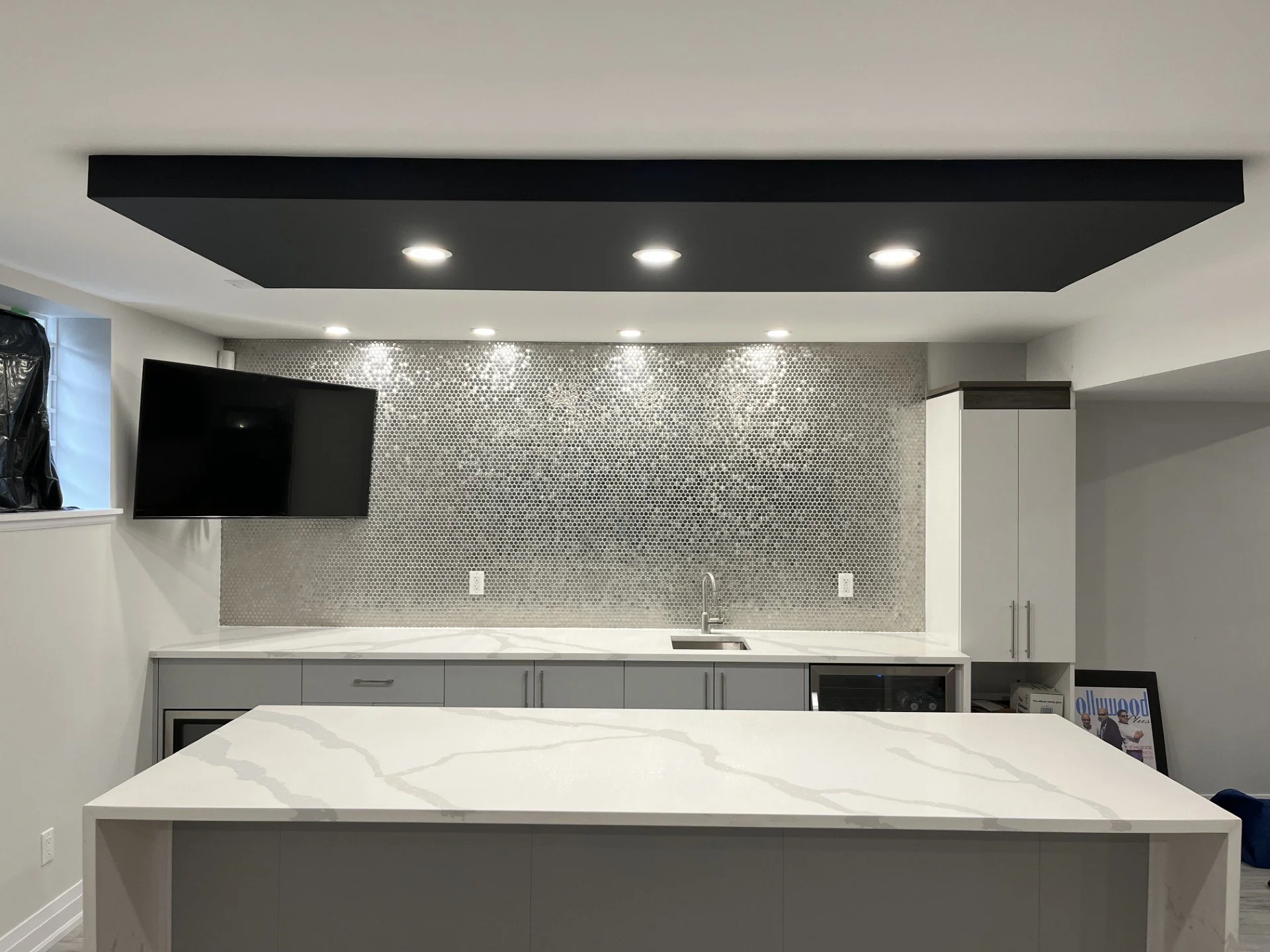 Modern kitchen with white marble island, gray cabinetry, mosaic tile backsplash, and black ceiling accent with recessed lighting.