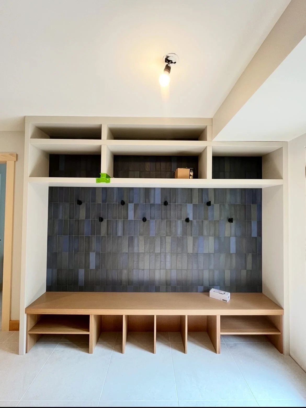 Contemporary built-in entertainment center with open shelves, a black tiled accent wall with hooks, and a wooden bench with cubbies beneath.