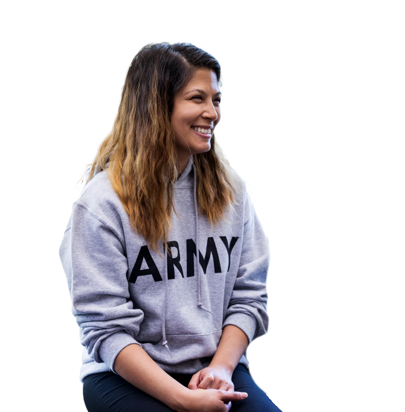 A young woman with light skin and long Wavy brown hair sitting and smiling, wearing a gray hoodie with 'ARMY' written on it.