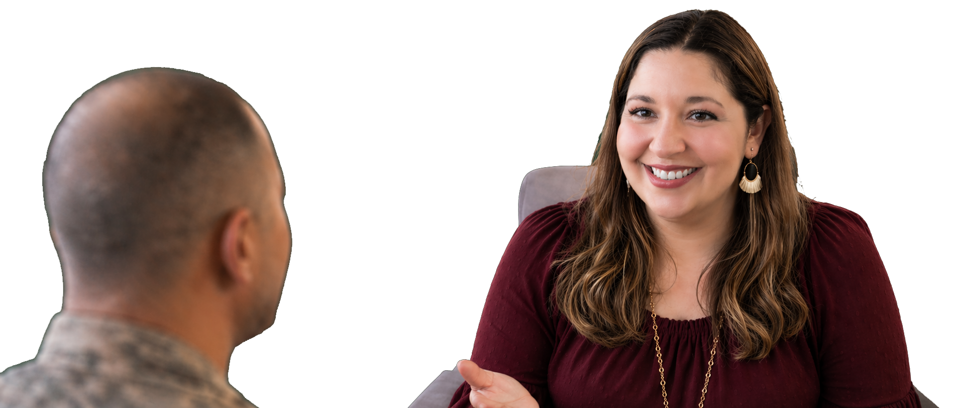 A woman with long brown hair smiling while talking to a man with a shaved head, seated in an indoor setting.