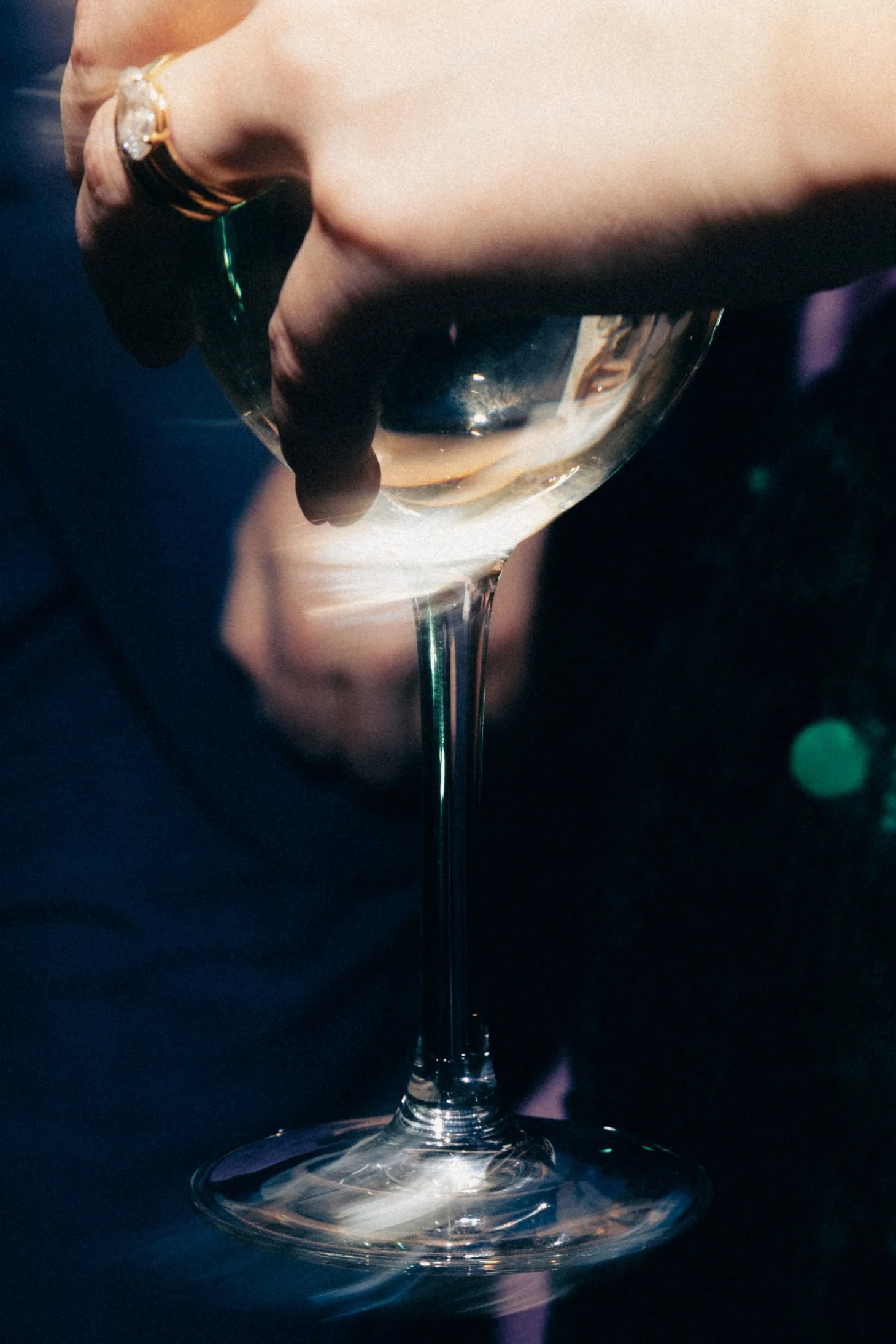 Close-up of a hand holding a wine glass filled with white wine, against a dark background.