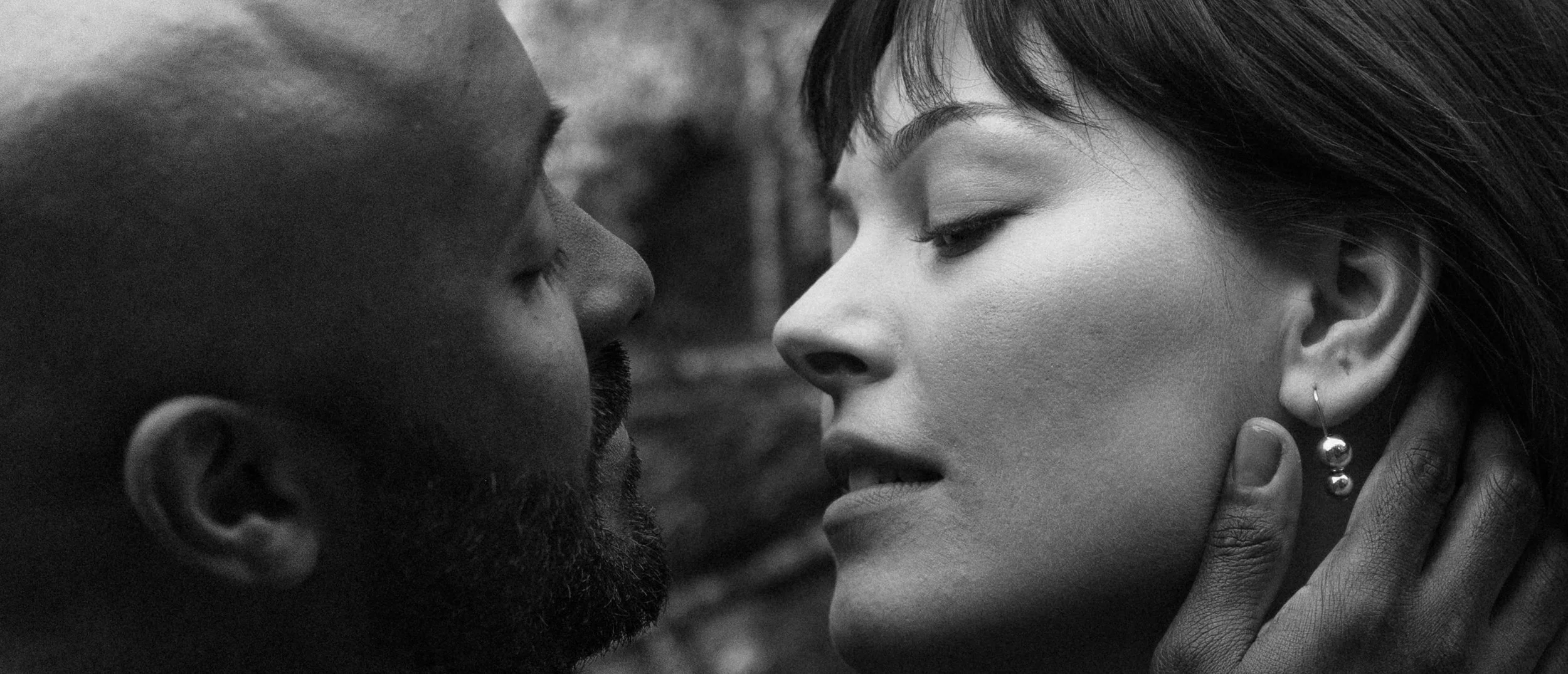 Close-up black and white photo of a man and woman with faces very close, touching foreheads, eyes closed, intimate moment.