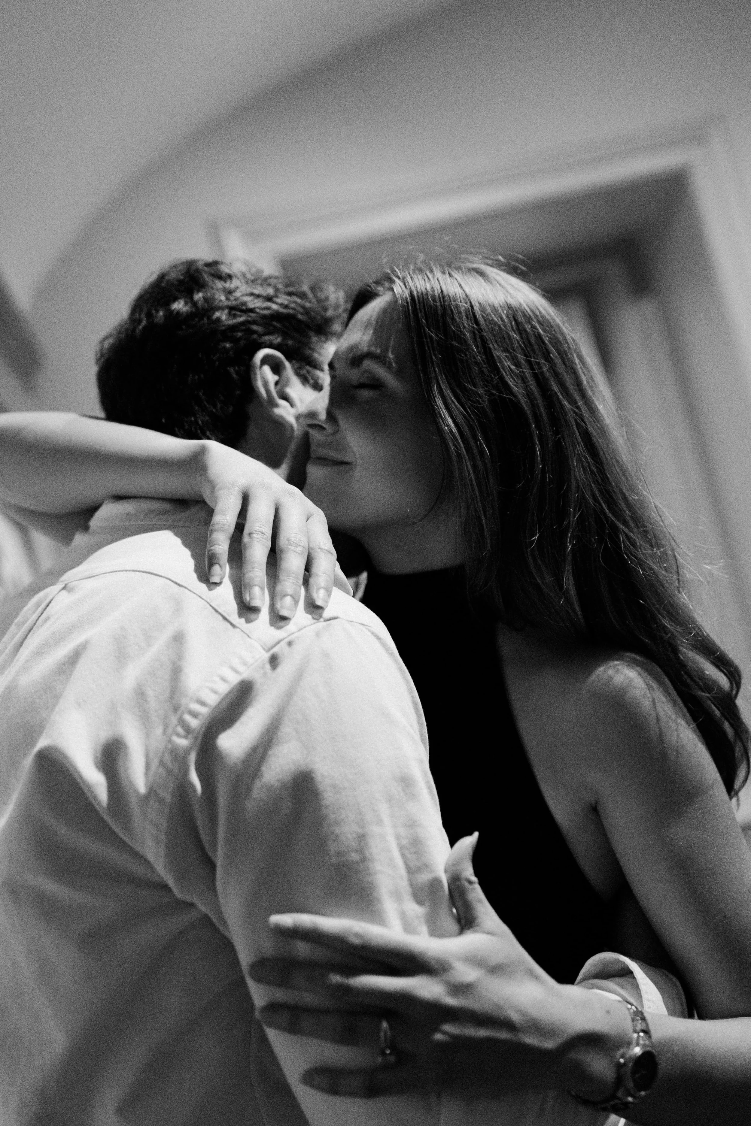 A black and white photo of a couple embracing. The woman is smiling with her eyes closed, and the man is facing her, holding her closely. The scene appears intimate and tender.