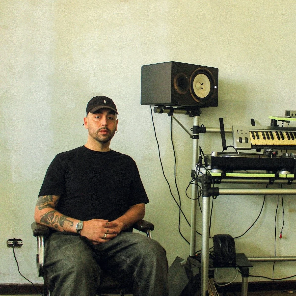 DJ ROOMPUNX from Curitiba at his studio. Man sitting in chair in a music studio with audio equipment, monitor speaker, and keyboard.