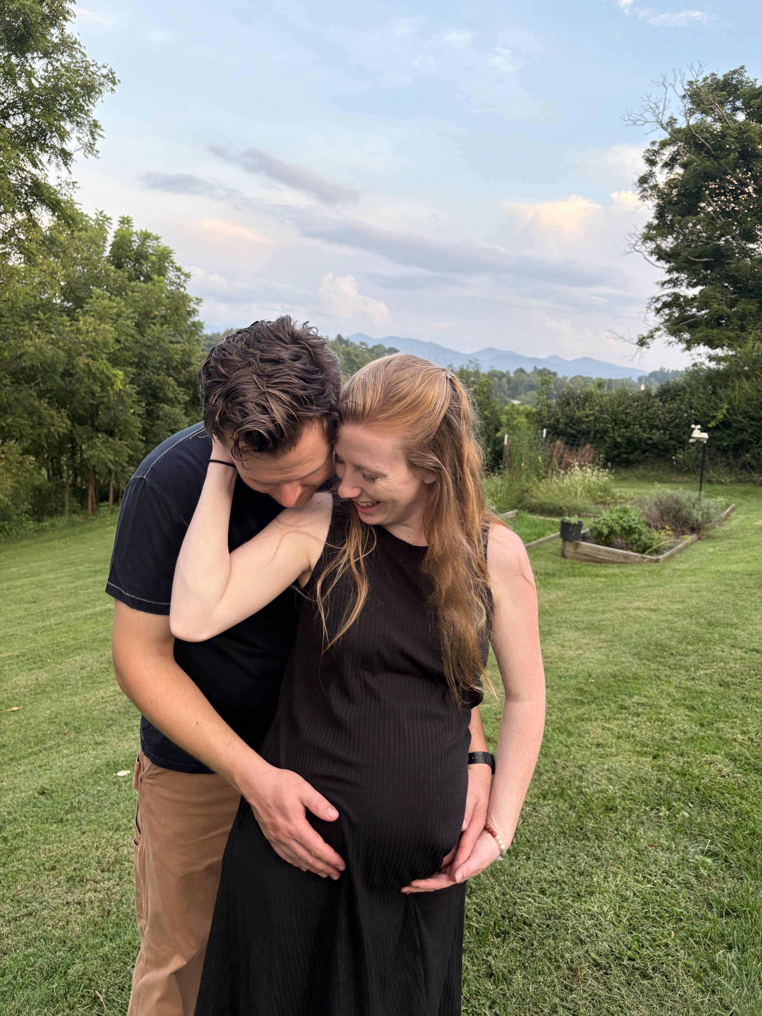 Sydney and Nolan Thompson embracing outdoors, with mountains and trees in the background, during daylight.