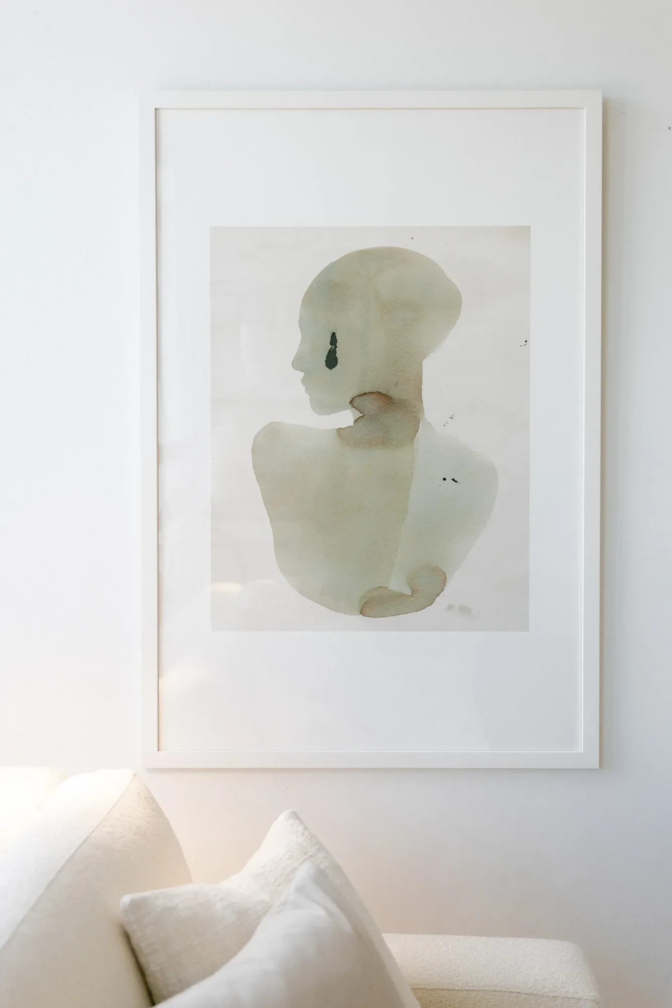 A watercolor painting in neutral color palette hangs over a cream couch