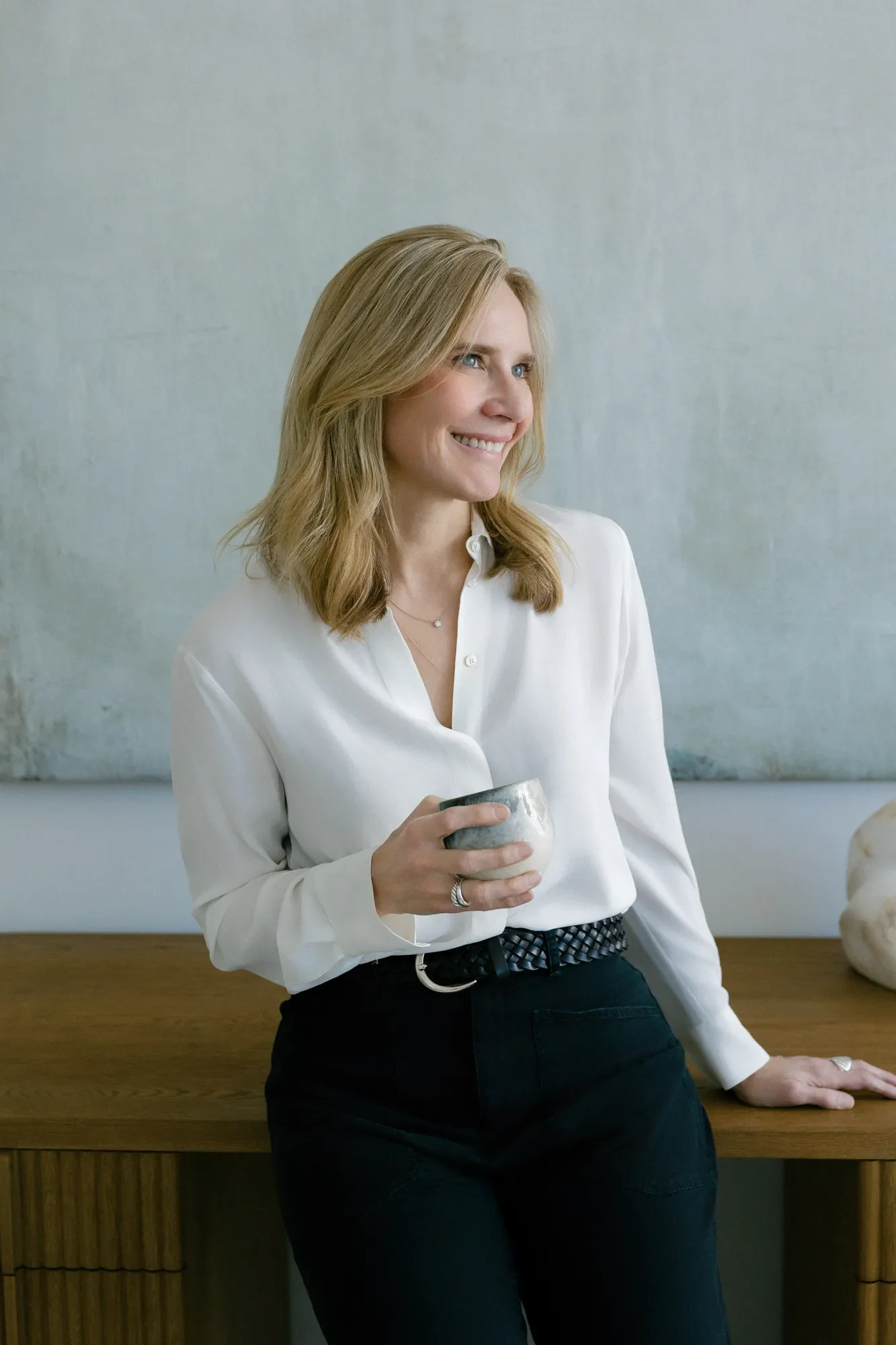 Therapist Jennifer Warpool in front of a large abstract painting, holding a mug and smiling