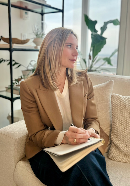 Therapist Jennifer Warpool in a camel-colored blazer writing notes on a couch