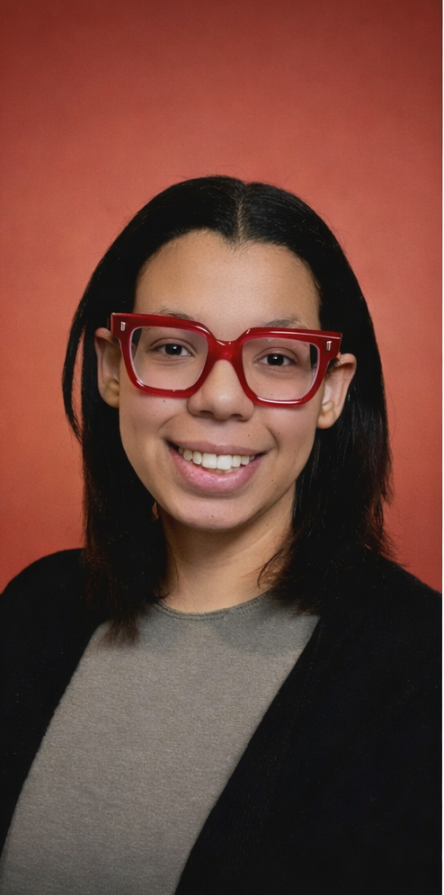 A young woman with medium skin tone, shoulder-length dark hair, and wearing red glasses, smiling against a reddish background.