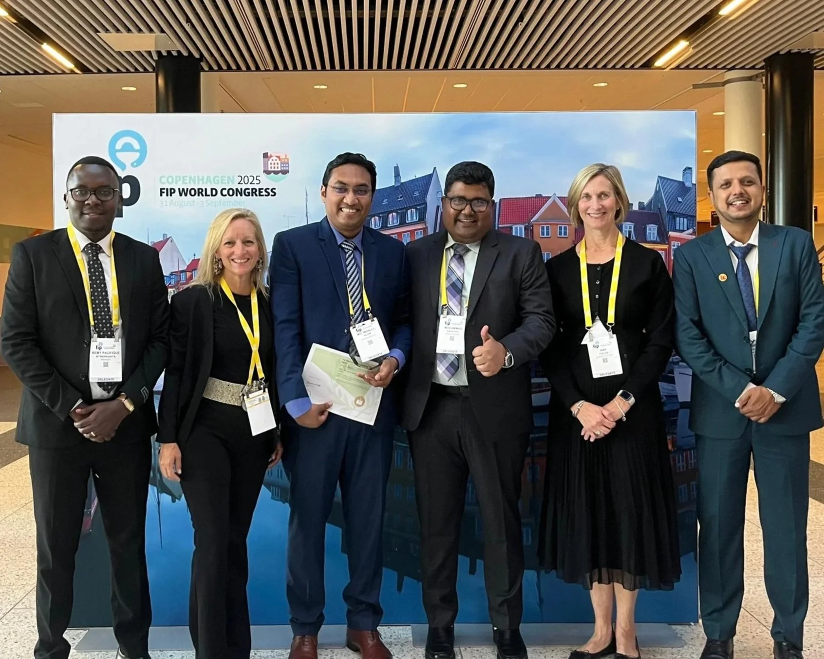 Six members fo the Vennue Global Leadership Team in business attire standing in front of a sign that reads 'Copenhagen 2025 FIP World Congress, 31 August - 5 September.'