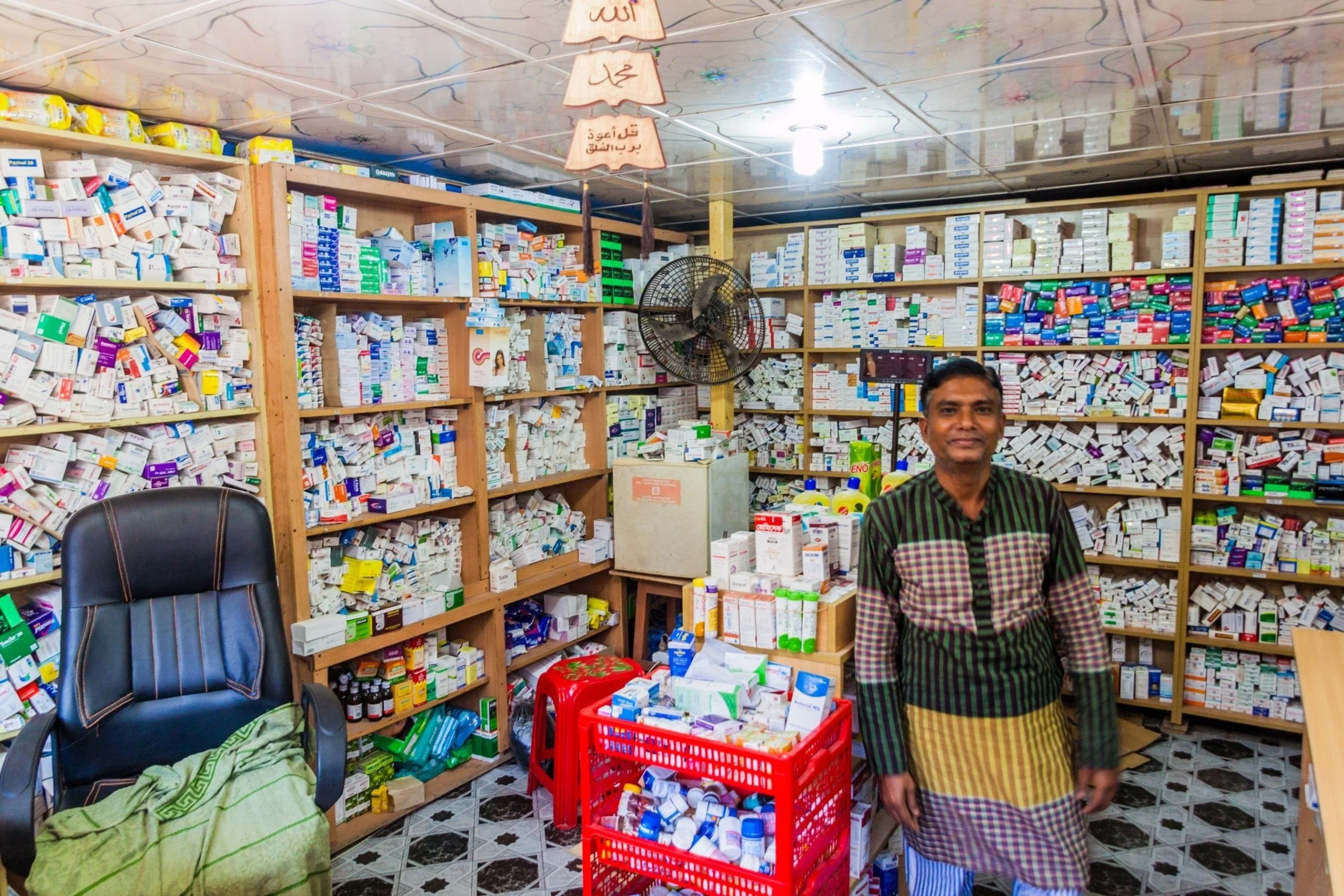 A man standing inside a pharmacy surrounded by shelves filled with medicines and pharmaceutical supplies.