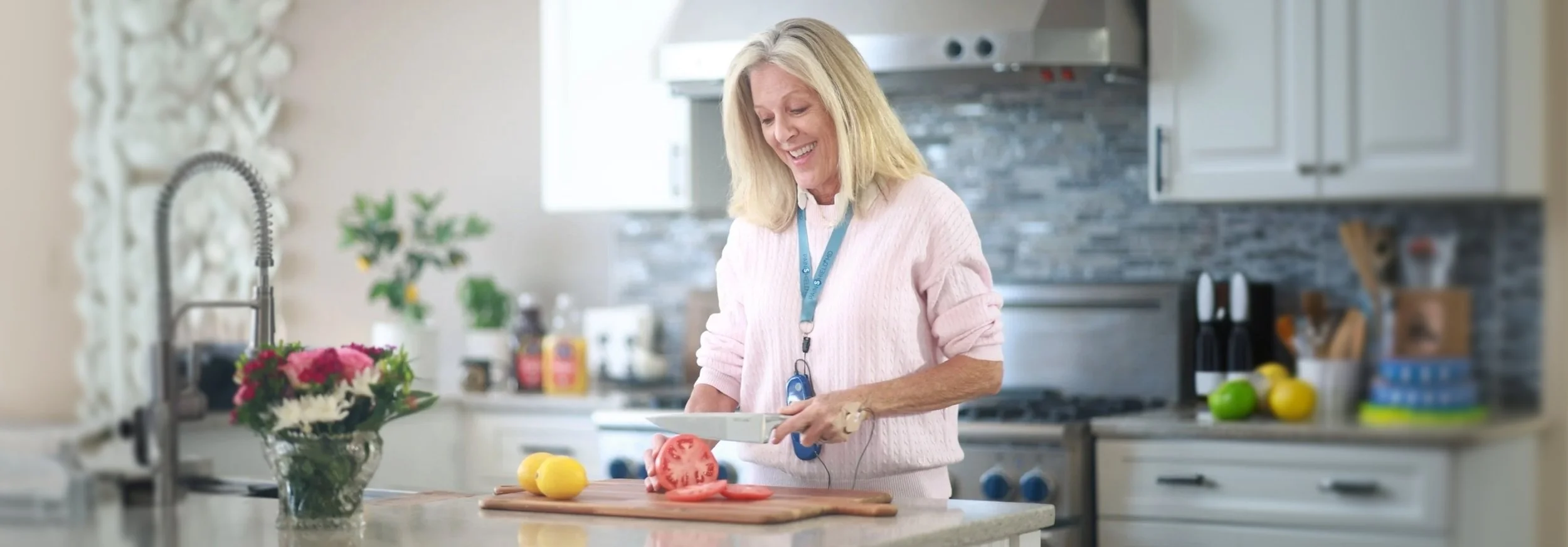 A woman chopping a tomato in a bright, modern kitchen with a bouquet of flowers on the counter.