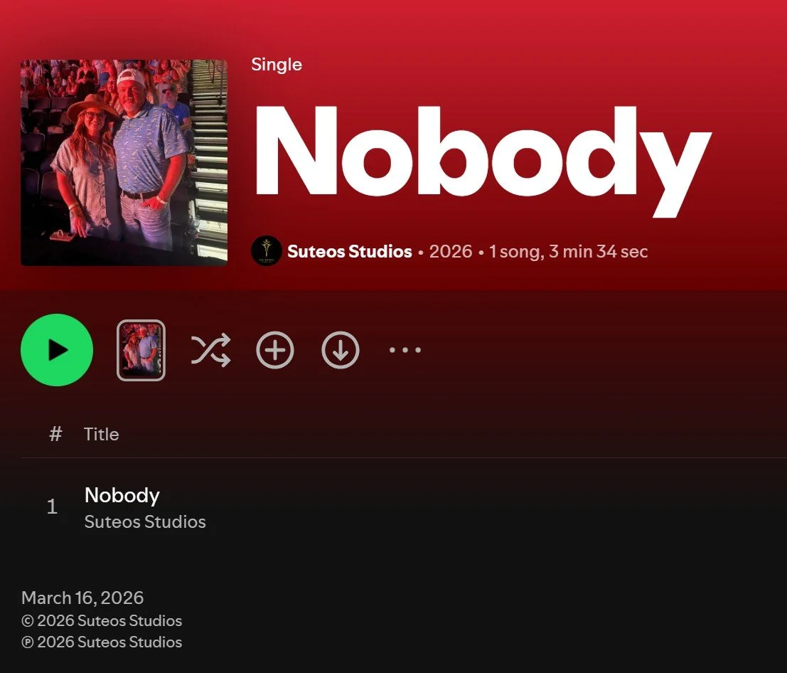 Music streaming app screen showing the song "Nobody" by Suteos Studios, released in 2026, with a cover image of two people at a concert or event, one wearing a hat, under a red background.
