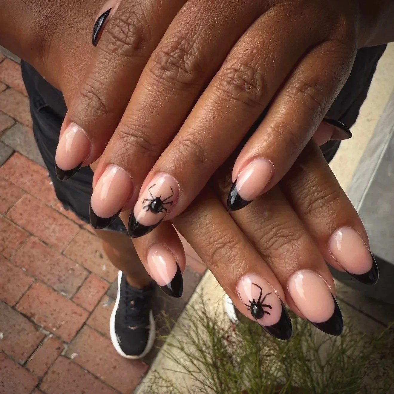 Close-up of manicured nails with black tips and spider nail art on each ring finger by Salon 230 Daytona Beach