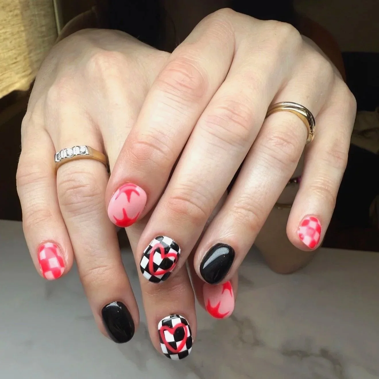 Woman's hands with various nail art, red and white checkered pattern nail art. another with a pink background and red crescent shapes, and black and white checkerboard patterns with red heart accents by Salon 230 Daytona Beach