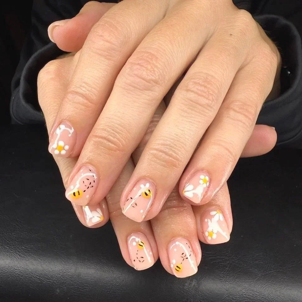 short manicured nails painted with floral and bee-themed nail art by Salon 230 Daytona Beach