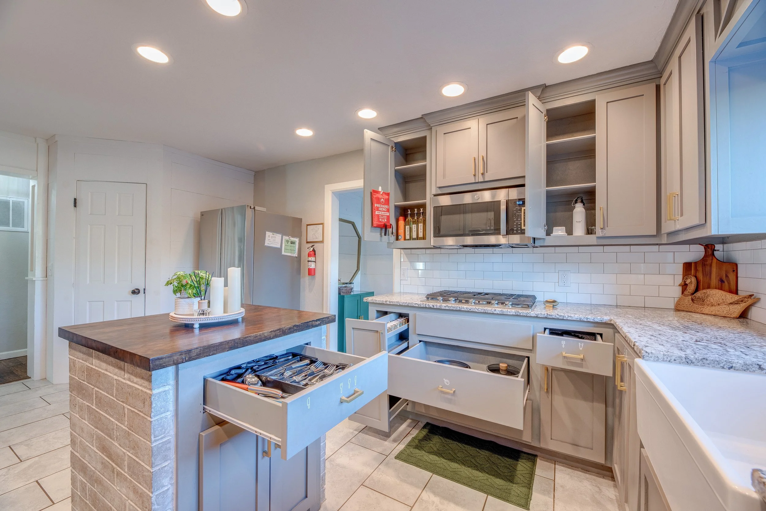 Modern kitchen with open cabinets, granite countertops, undermount sink, stainless steel microwave, and appliances, with a kitchen island and decorative items.