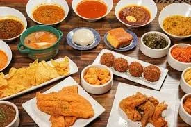 A table featuring many plates and bowls of different southeren food incluidng freid fish, corn bread, beans