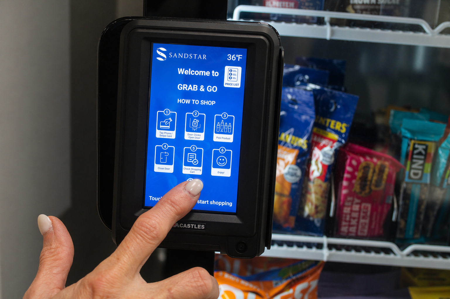 Person using a touchscreen kiosk in a vending area with snack bags visible in the background.