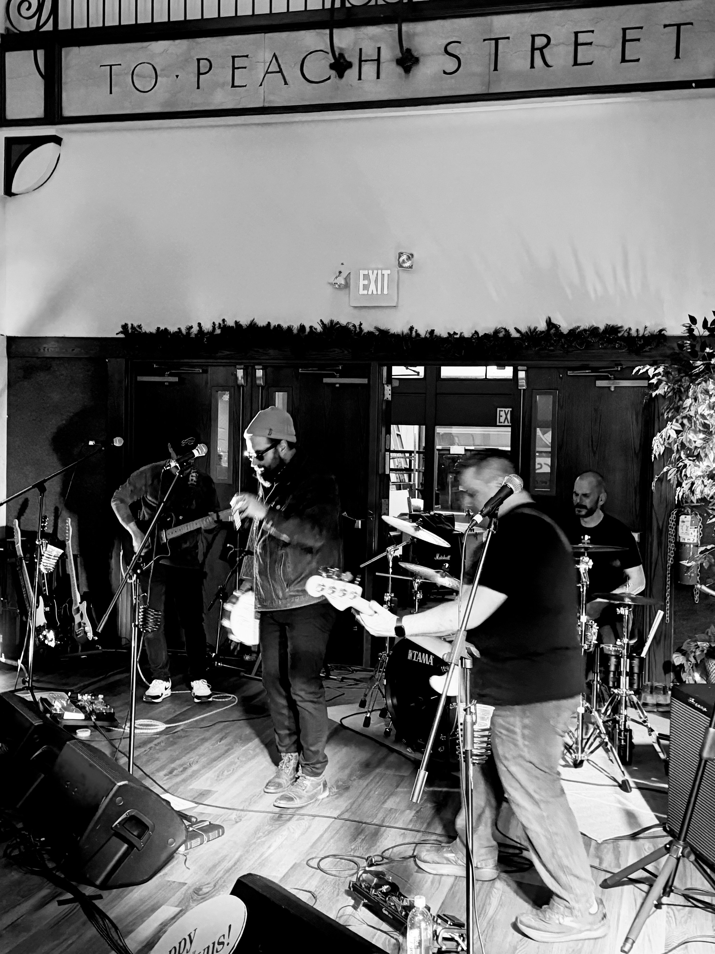 A band performing live on stage with musical instruments, including guitars and drums, in a venue with a sign that reads 'TO PEACH STREET'.