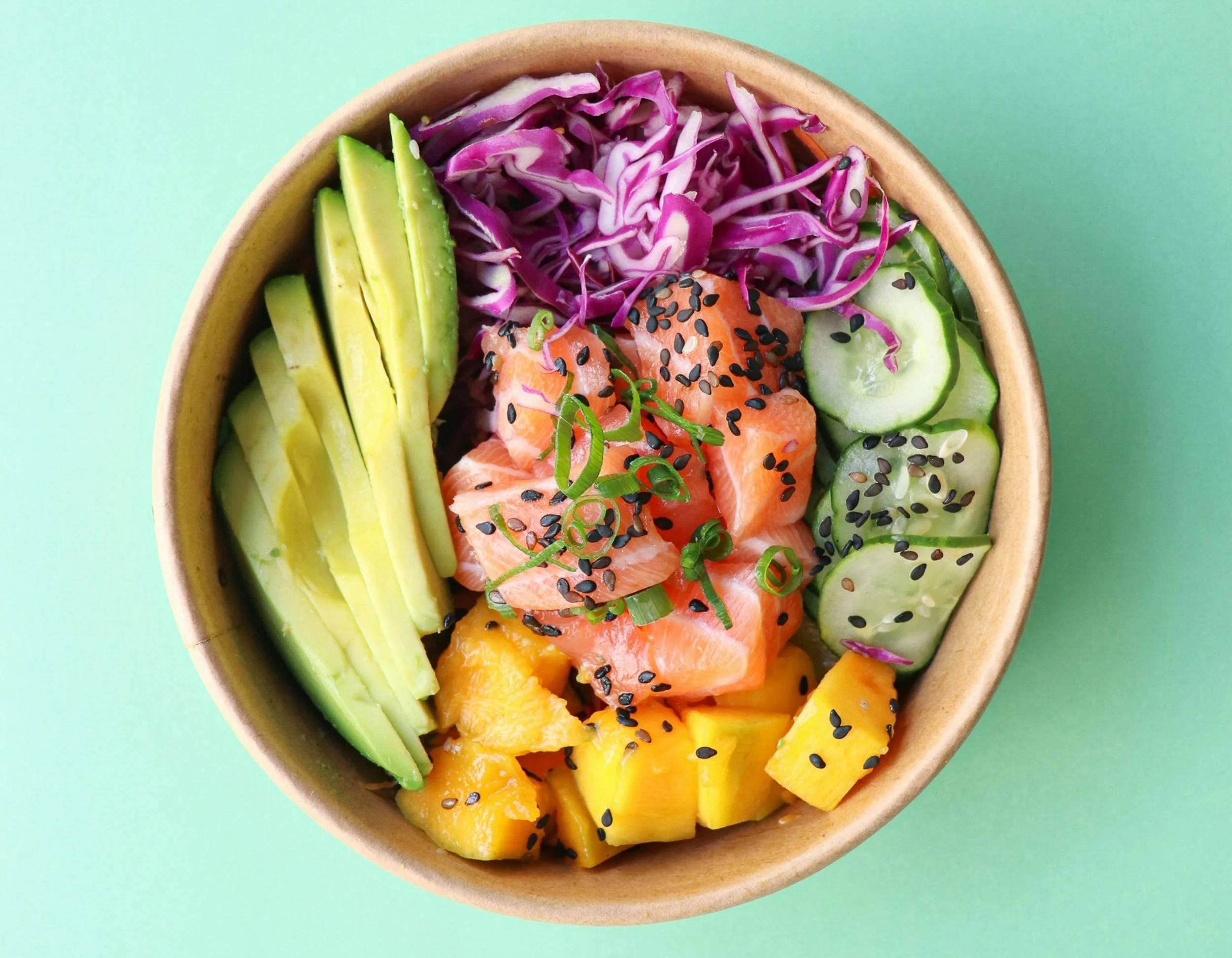 Obst- und Gemüsesalat in einer Schüssel mit Lachs, Avocado, Gurke, Mango, Rotkohl, Frühlingszwiebeln und schwarzem Sesam.