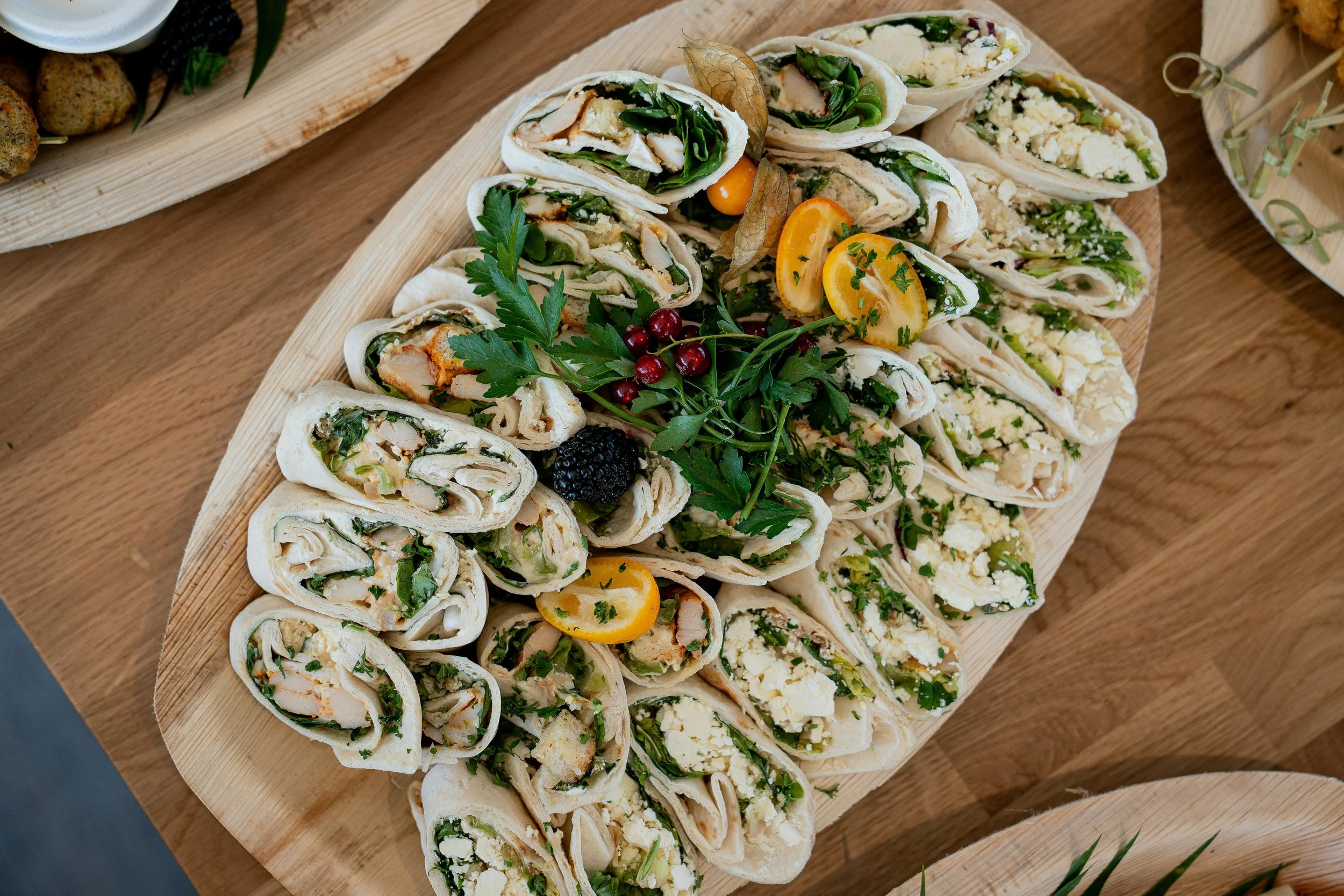 Verschiedene gefüllte Wraps mit Gemüse, Käse und Kräutern, dekoriert mit Beeren und Zitronenscheiben, auf einem Holzbrett serviert.