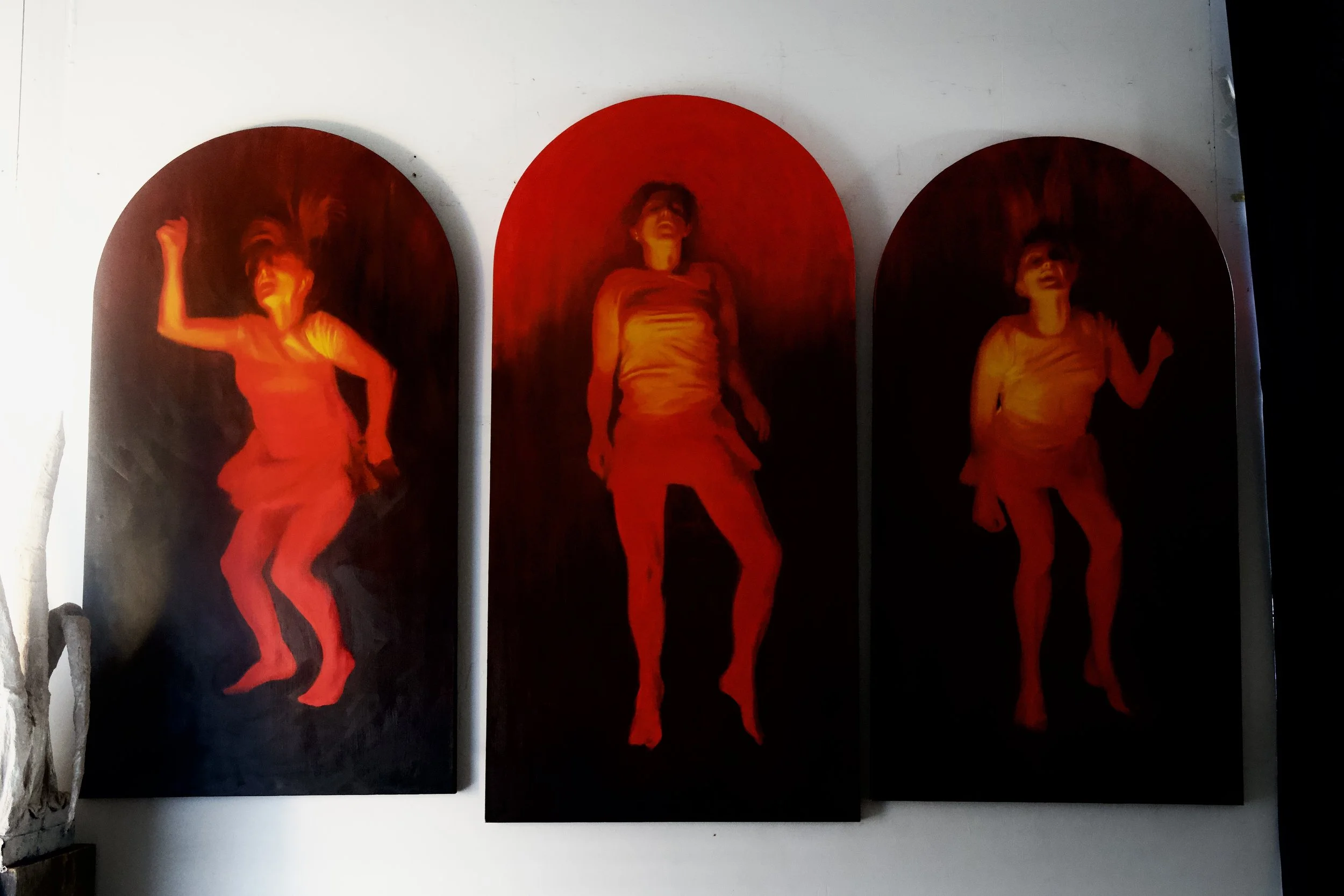 Triptych of three paintings featuring a woman in different poses, all in red tones with dark backgrounds.